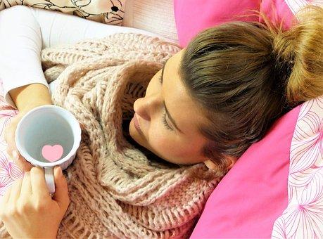 En kvinna som ligger mot en rosa dyna och dricker te.