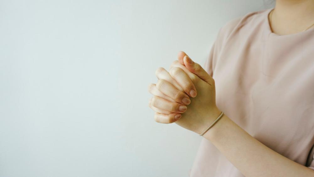 En kvinna som knäpper sina händer i bön.