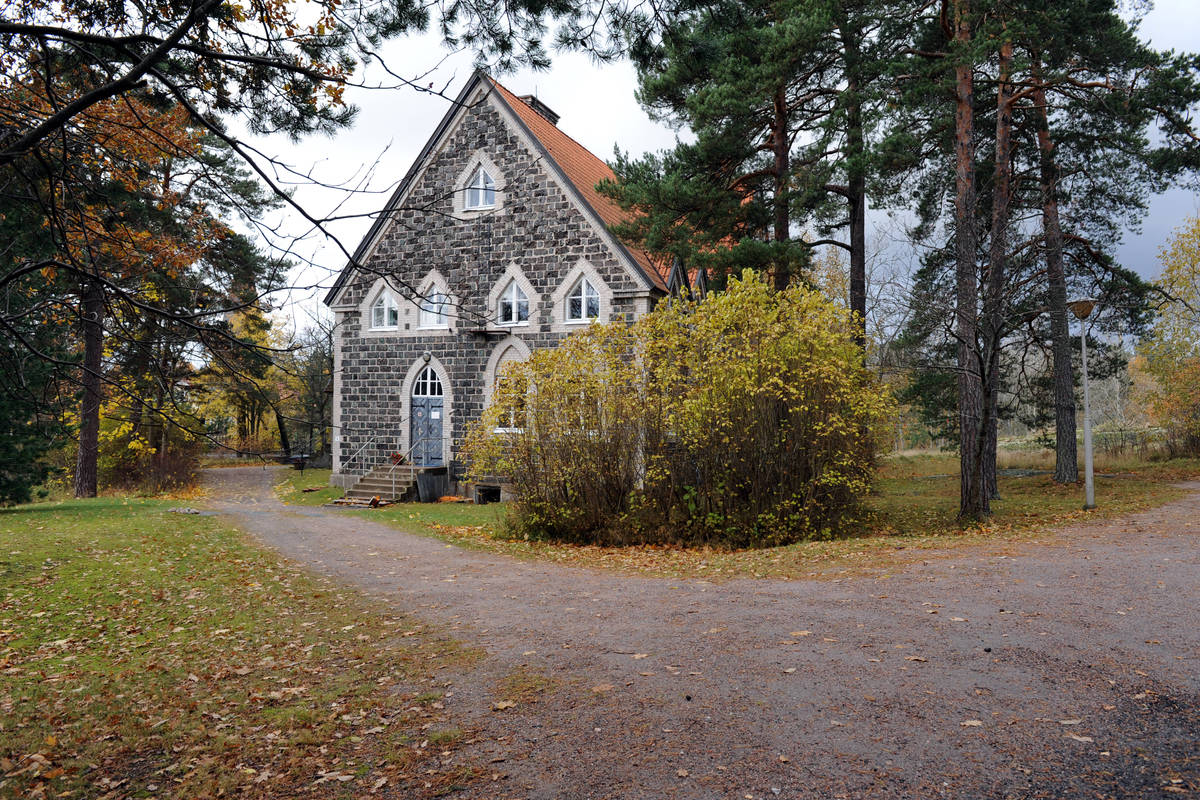 Dalsbruks stenkyrka omgiven av tallar och bladträd och buskar i höstskrud.