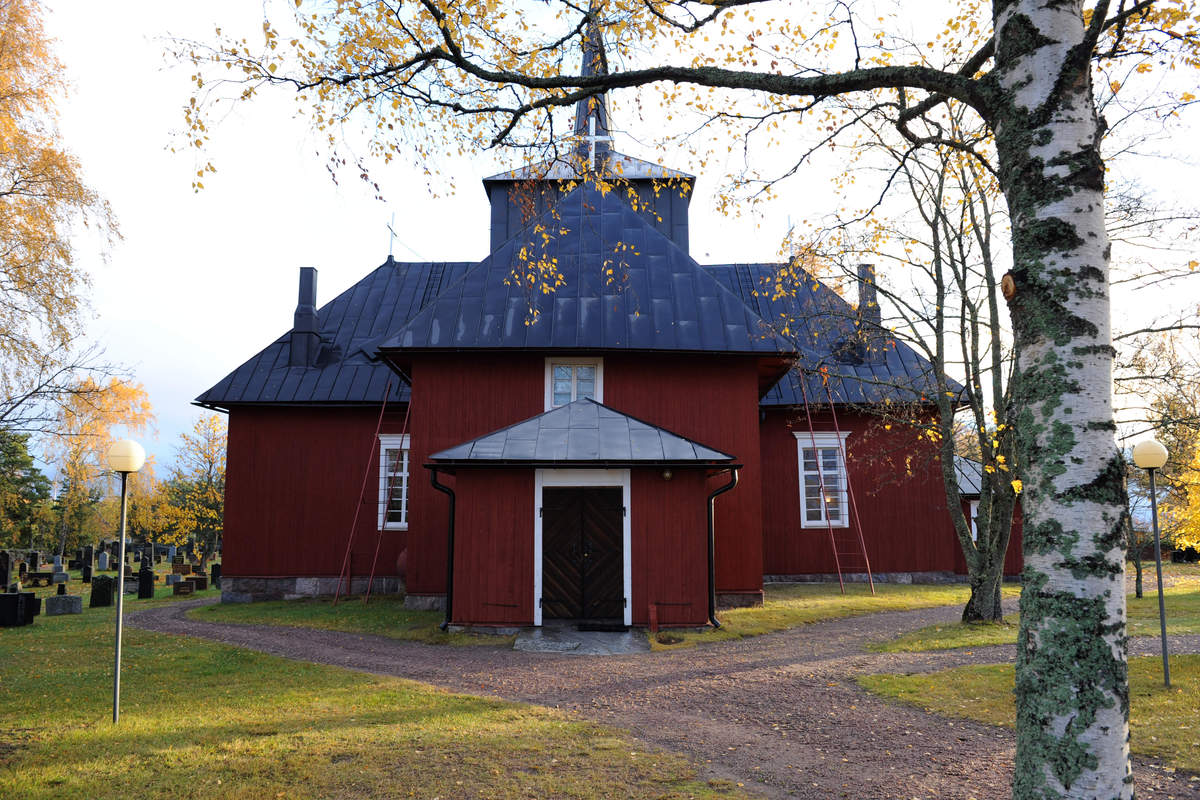 Hitis röda träkyrka bland björklöv på hösten.