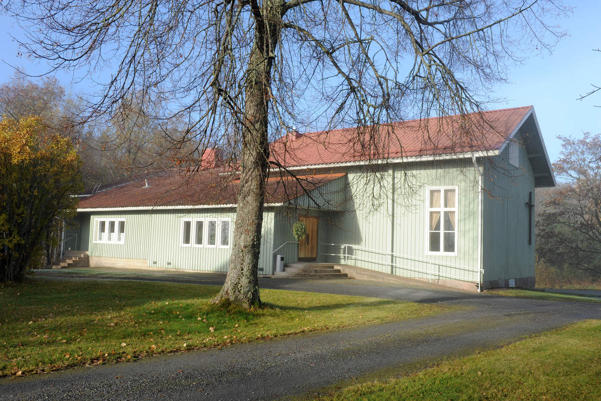 Församlingshemmet i Kimito som har gröna väggar och rött tak. I förgrunden ett stort träd som redan fällt sina löv. 