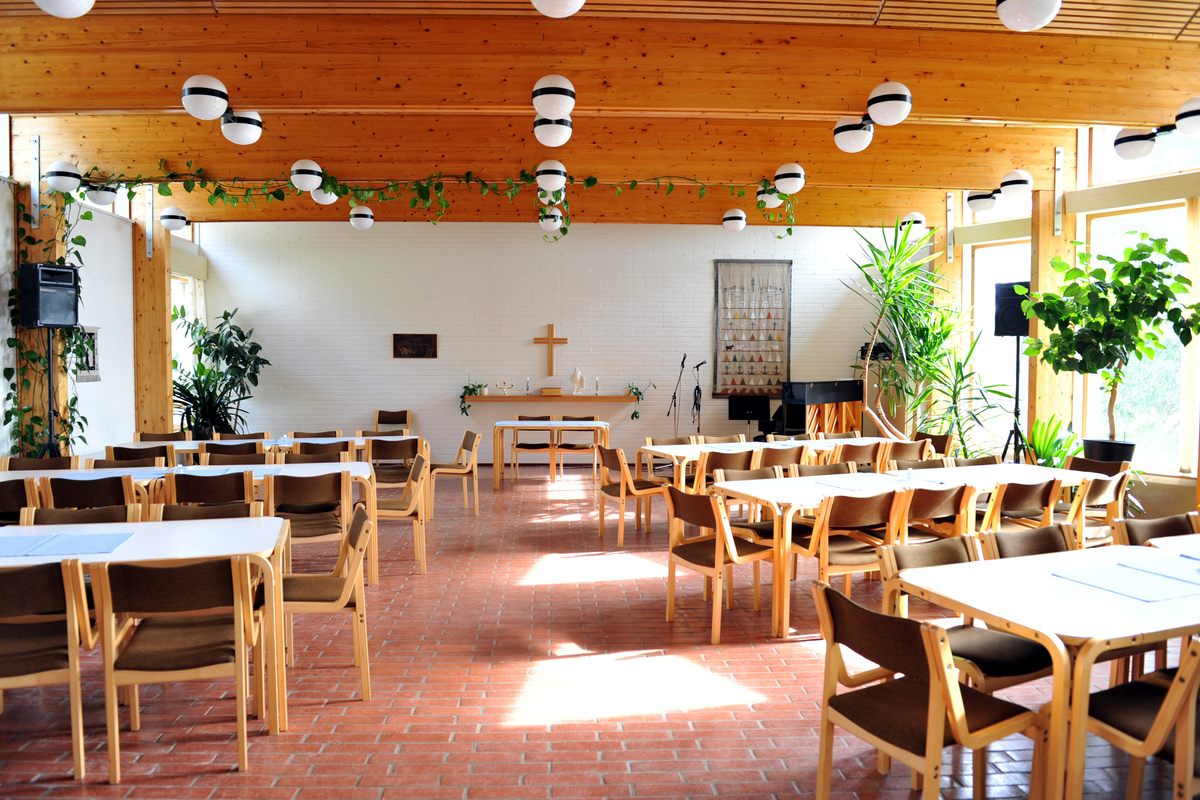 Solljuset lyser in i Västanfjärds församlingshem. Församlingshemmet har tegelgolv och träbalkar i taket. I salen finns bord, stolar och flera grönväxter.